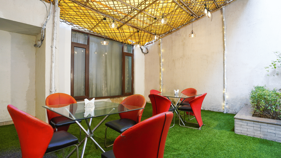Outdoor courtyard cafe showing two table sets with red chairs beneath a bamboo-lattice canopy strung with fairy lights.