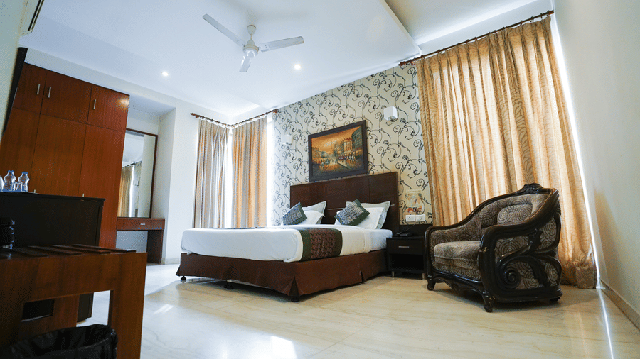 Guest room with a dark headboard, a framed Parisian painting, gold curtains, green cushions, a dark minibar, and a ceiling fan.