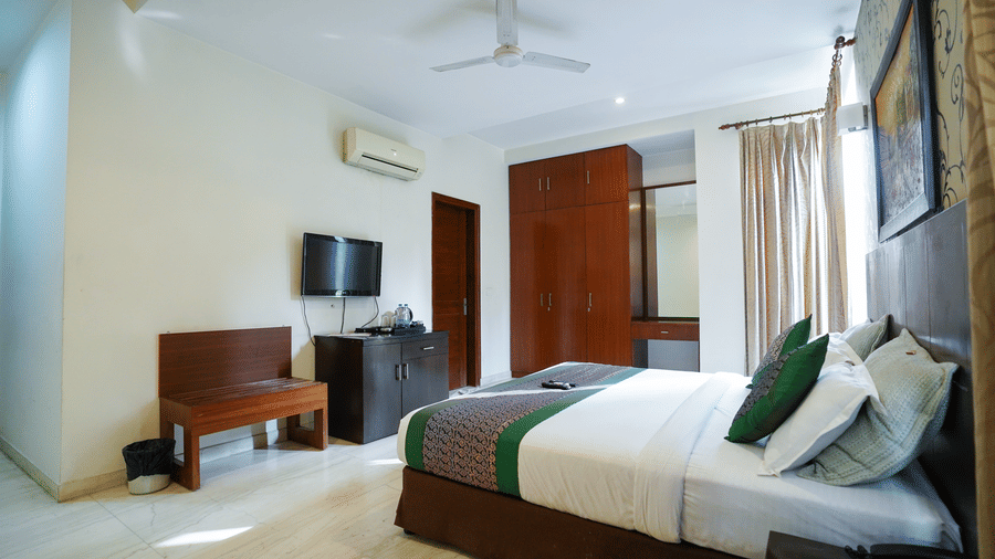 An image of a bedroom featuring a bed, a bedside table, a flat TV screen, a bench, a cabinet, and a wardrobe - Lime Tree Hotel, Iffco Chowk 