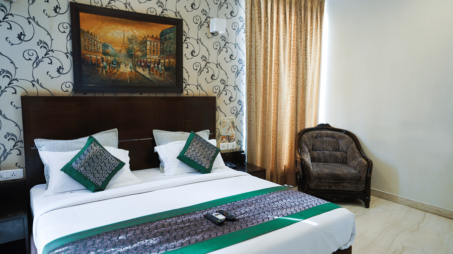 Double bed with crisp linens, elegant patterned walls, a cosy armchair and warm natural light for a relaxing st