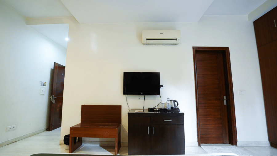 Guest room detail with a wall-mounted LG TV, a split air conditioner, a dark minibar with electric kettle, and a luggage rack.