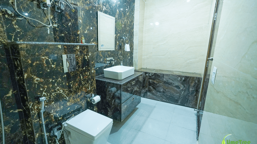 Bathroom with black and gold marble walls, a wall-hung toilet, white vessel sink, mirror, and glass shower partition at Lime Tree Hotel Near 32nd Avenue.