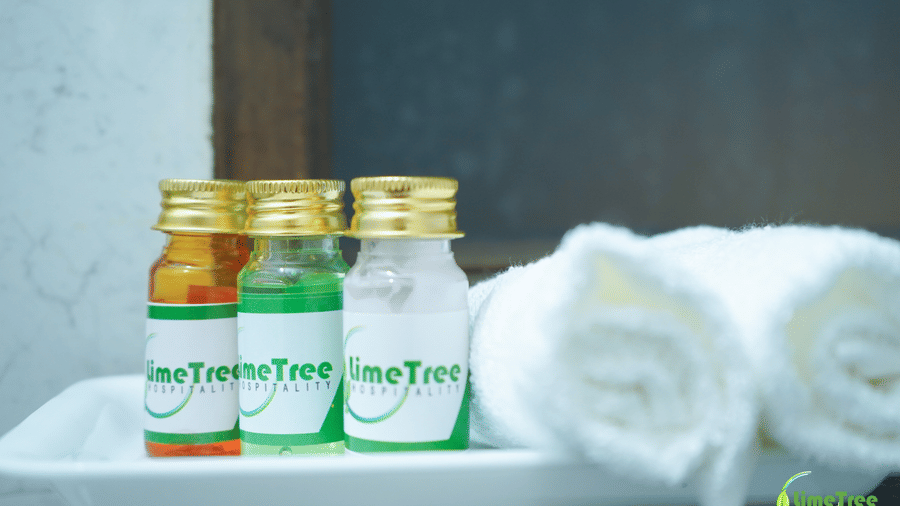 3 LimeTree Hospitality toiletry bottles with gold caps on a white bathroom tray beside a rolled towel at Lime Tree Hotel Near 32nd Avenue.