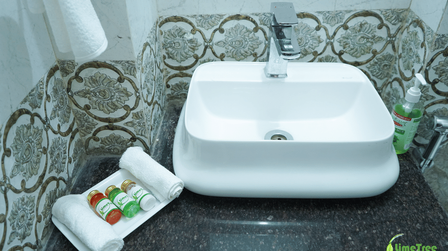 Bathroom vanity with a white vessel sink, patterned grey and gold tile, and LimeTree bath amenities on a tray at Lime Tree Hotel Near 32nd Avenue.