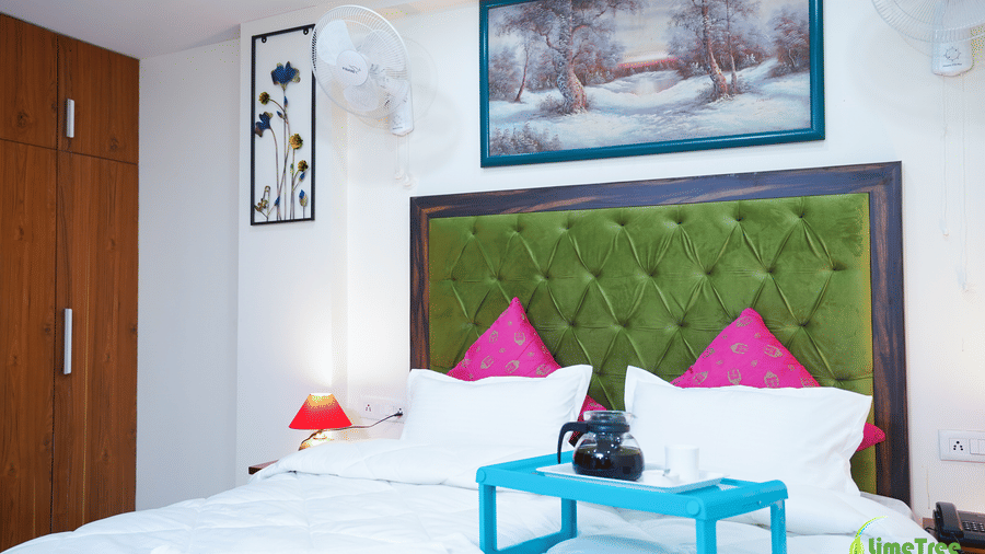 Guest room bed with a green tufted headboard, pink cushions, and a blue breakfast tray holding a coffee pot at Lime Tree Hotel Near 32nd Avenue.
