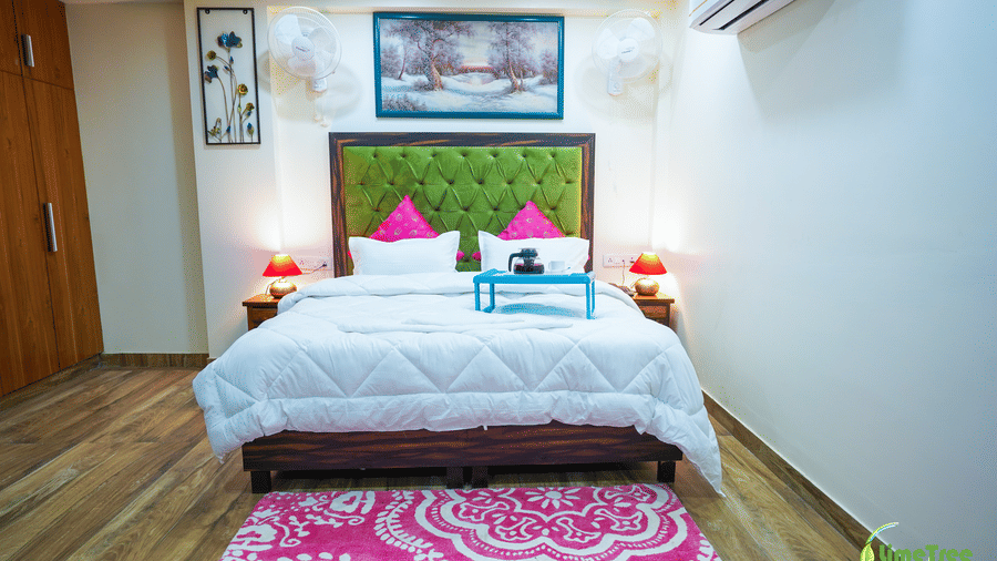Guest room bed with a green tufted headboard, pink cushions, a blue breakfast tray, and a pink patterned rug at Lime Tree Hotel Near 32nd Avenue.