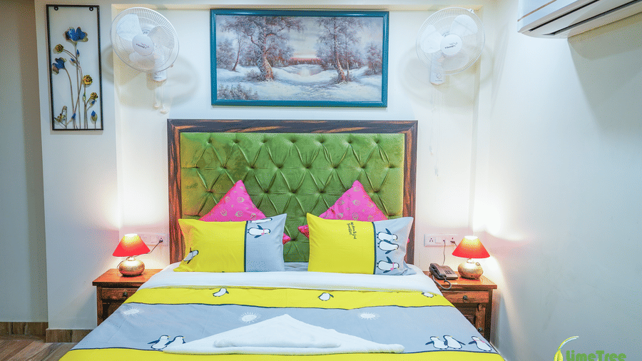 Bedroom at Lime Tree Hotel Near 32nd Avenue with a green tufted headboard, a snowy forest painting, 2 wall fans, red table lamps, and cushions.
