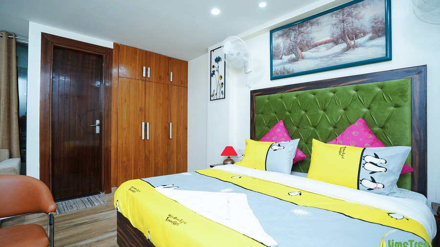 Bedroom at Lime Tree Hotel Near 32nd Avenue with a green tufted headboard, a snowy forest painting, a wooden wardrobe, and a tan leather chair.