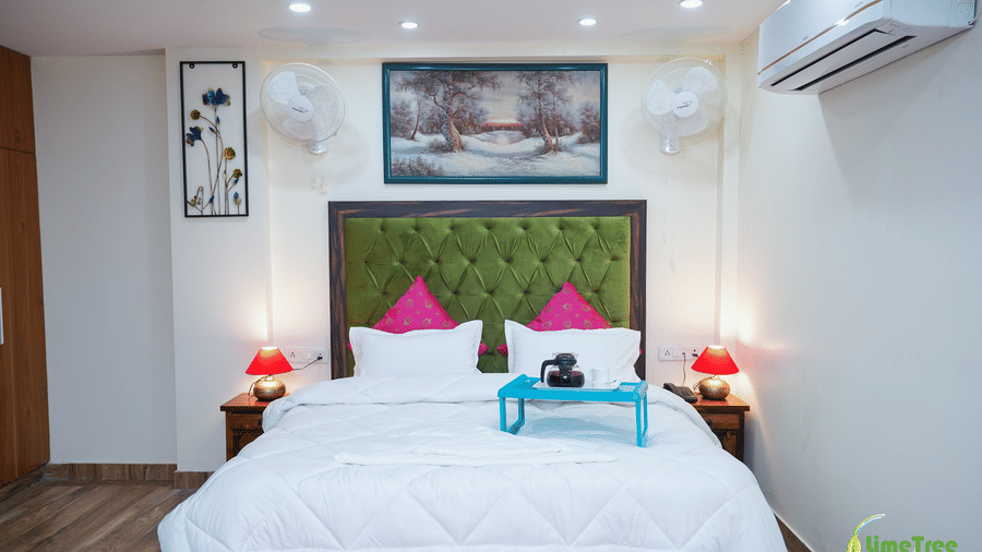 Guest room at Lime Tree Hotel Near 32nd Avenue with a green tufted headboard, a blue breakfast tray with a kettle, 2 red lamps, wall fans, and a snow painting.