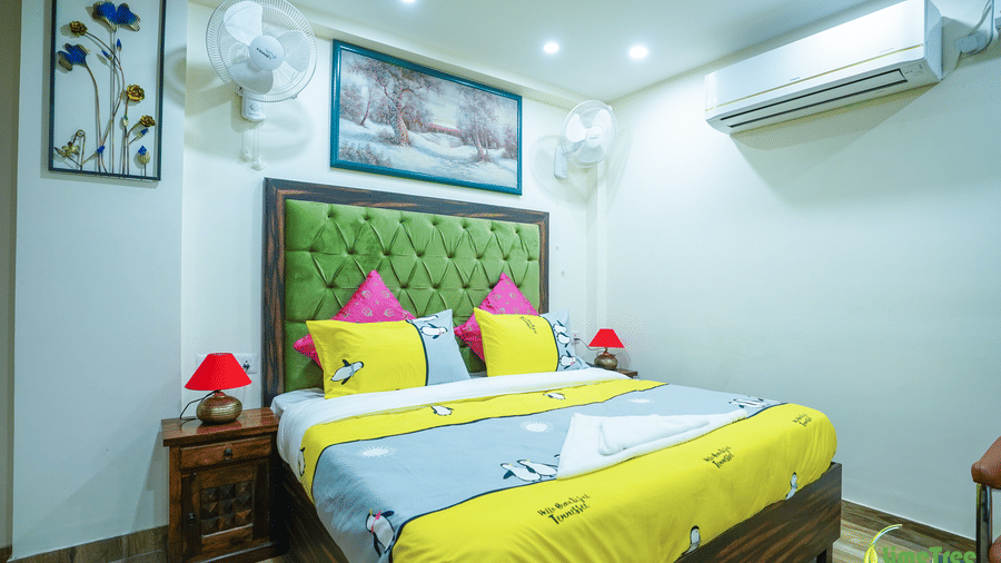 Guest room at Lime Tree Hotel Near 32nd Avenue with a green tufted headboard, penguin-print bedding, pink cushions, 2 wall fans, a winter painting, and AC