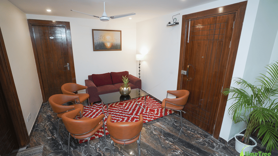 Lounge landing at Lime Tree Hotel Near 32nd Avenue with a maroon sofa, 4 tan leather chairs, a glass table, a red rug, and a potted palm.
