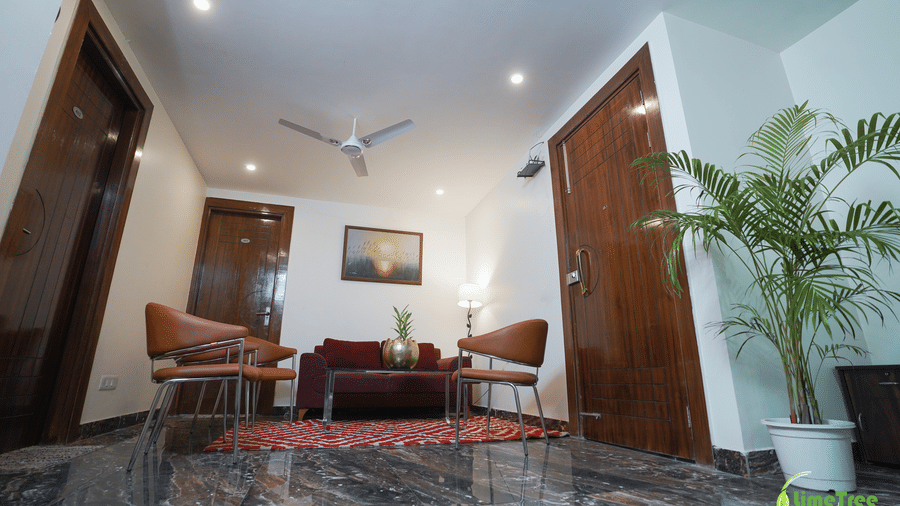 Lounge landing at Lime Tree Hotel Near 32nd Avenue with a maroon sofa, 3 tan leather chairs, a red rug, a potted palm, and wooden doors.