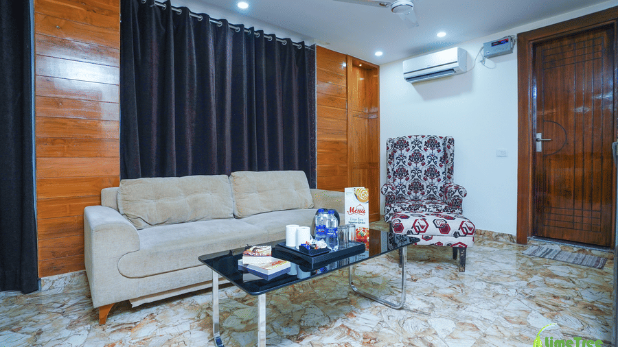 Seating area with a beige sofa, damask wingback chair, and a glass table holding a Signature Kitchen menu card at Lime Tree Hotel Near 32nd Avenue.