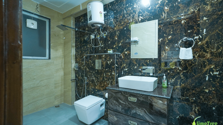 Bathroom with black and gold marble walls, a white toilet, vessel sink, mirror, wall geyser, and towel ring at Lime Tree Hotel Near 32nd Avenue.