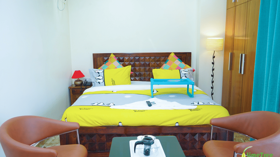 Guest room at Lime Tree Hotel Near 32nd Avenue with a king bed, colorful pillows, a brown sofa, a wooden coffee table, and marble flooring