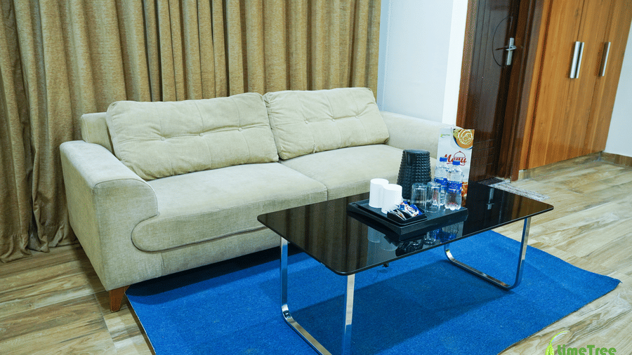 A cream-coloured sofa positioned next to a black glass coffee table on a vibrant blue rug over wooden flooring.