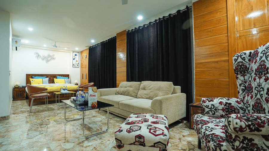 Studio suite at Lime Tree Hotel Near 32nd Avenue with a beige sofa, patterned ottoman, damask armchair, a glass table with a menu, and a bed in the background