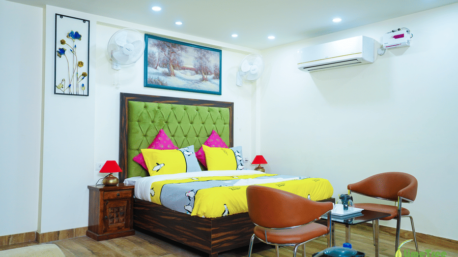Studio suite at Lime Tree Hotel Near 32nd Avenue with a green-headboard bed, 2 tan leather chairs, a glass table, and a wardrobe on a blue rug.