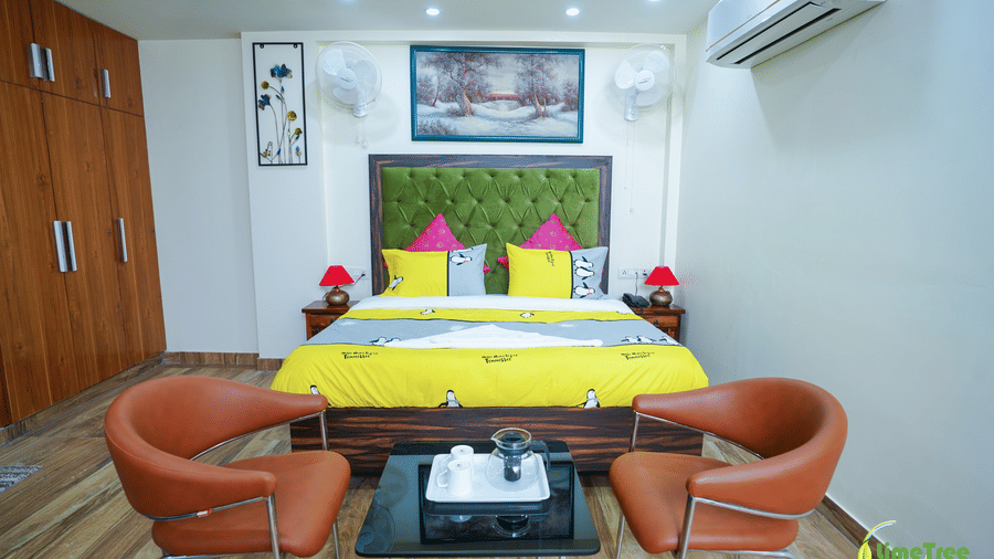 Studio suite at Lime Tree Hotel Near 32nd Avenue with a beige sofa, 2 tan leather chairs, a glass table, and a green-headboard bed on a blue rug.