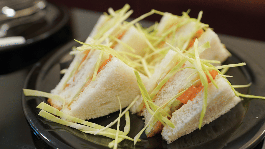 Grilled vegetable sandwich sliced into triangles with a green-and-white filling and shredded cabbage on top, presented on a black plate over a dark surface.