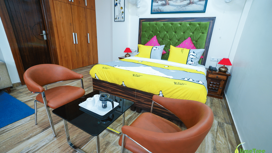 A hotel bedroom featuring a double bed dressed in vibrant yellow linens, flanked by two brown armchairs and a coffee table.