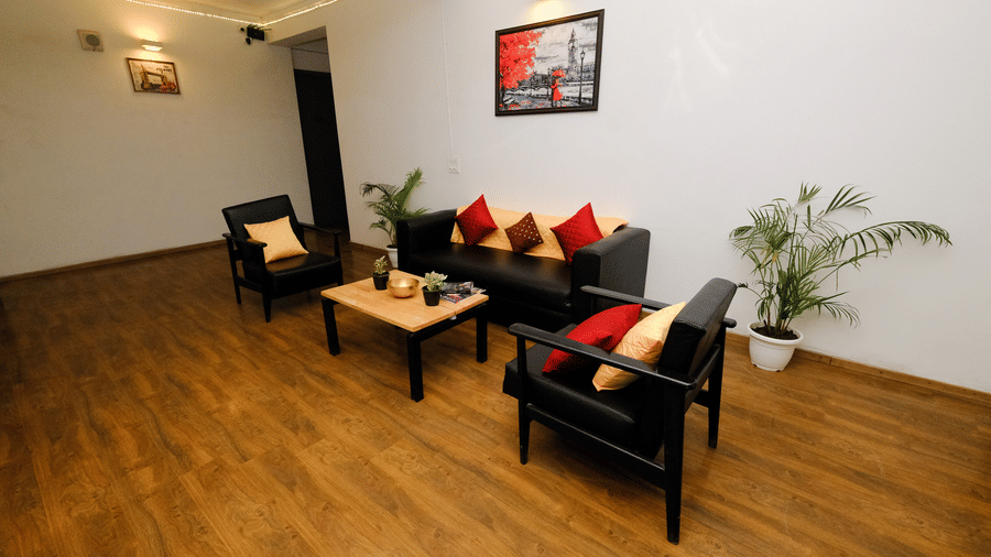 Lounge area of Lime Tree Hotels & Service Apartment Private Limited featuring black sofas, red cushions, and wooden flooring.