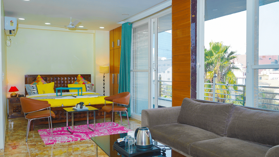 Living room of Lime Tree Hotels & Service Apartment Private Limited featuring colourful sofas, a glass wall, and floor to ceiling windows.