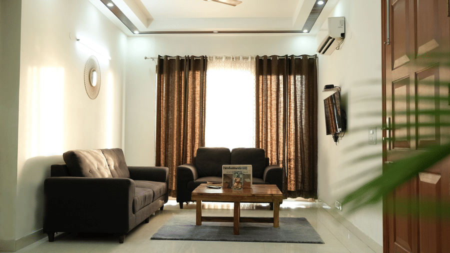 Lounge area of Lime Tree Hotels & Service Apartment Private Limited featuring a dark sofa, a potted plant, and framed wall art.