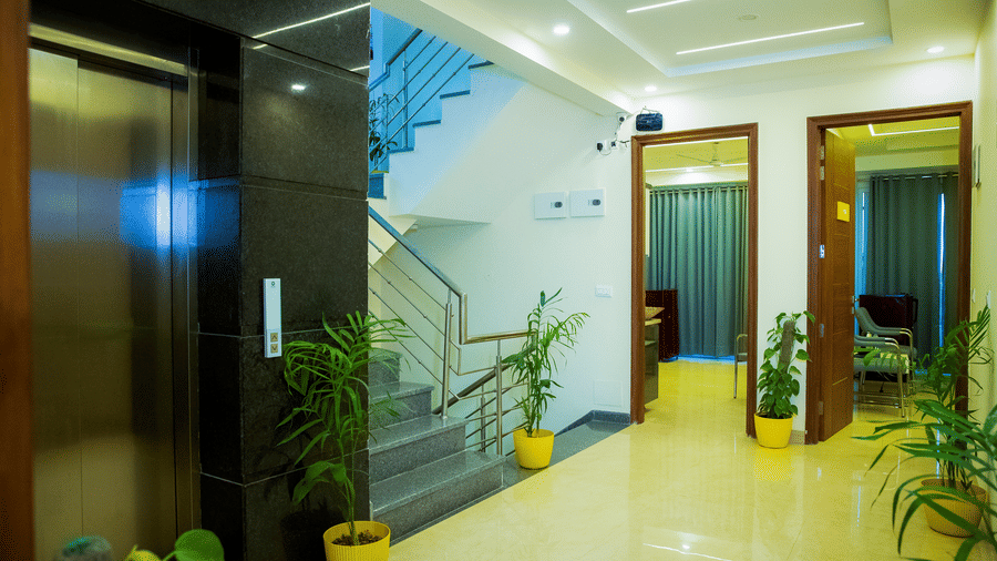 Corridor of Lime Tree Hotels & Service Apartment Private Limited featuring a lift, potted plants, and wooden doors.