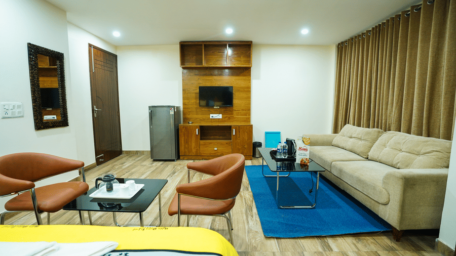 Living room of Lime Tree Hotels & Service Apartment Private Limited featuring an orange sofa, a blue coffee table, and framed wall art.