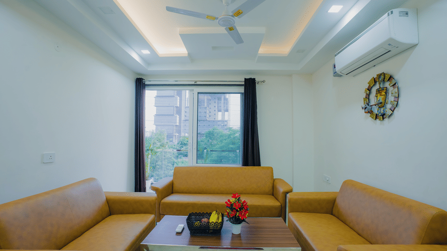 Lounge area of Lime Tree Hotels & Service Apartment Private Limited featuring an orange sofa, a wall clock, and a coffee table.