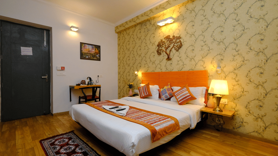 Bedroom of Lime Tree Hotels & Service Apartment Private Limited featuring an orange throw, patterned wallpaper, and bedside lamps.