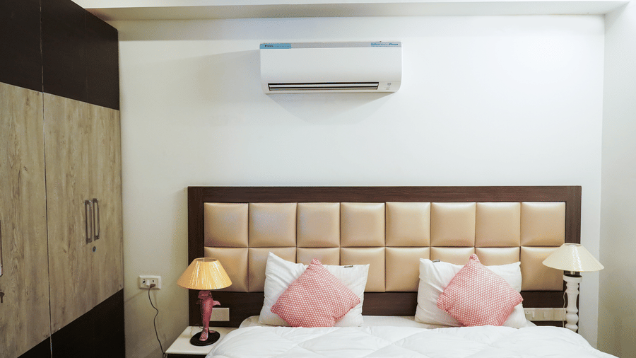 Bedroom of Lime Tree Hotels & Service Apartment Private Limited featuring pink cushions, a padded headboard, and an air conditioning unit.
