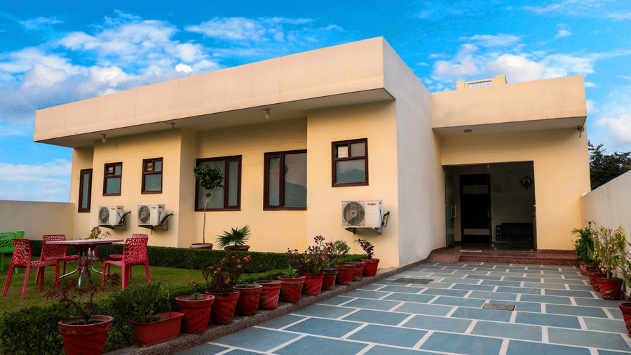 Single storey building exterior of Lime Tree Hotels & Service Apartment Private Limited featuring a paved courtyard and potted plants.