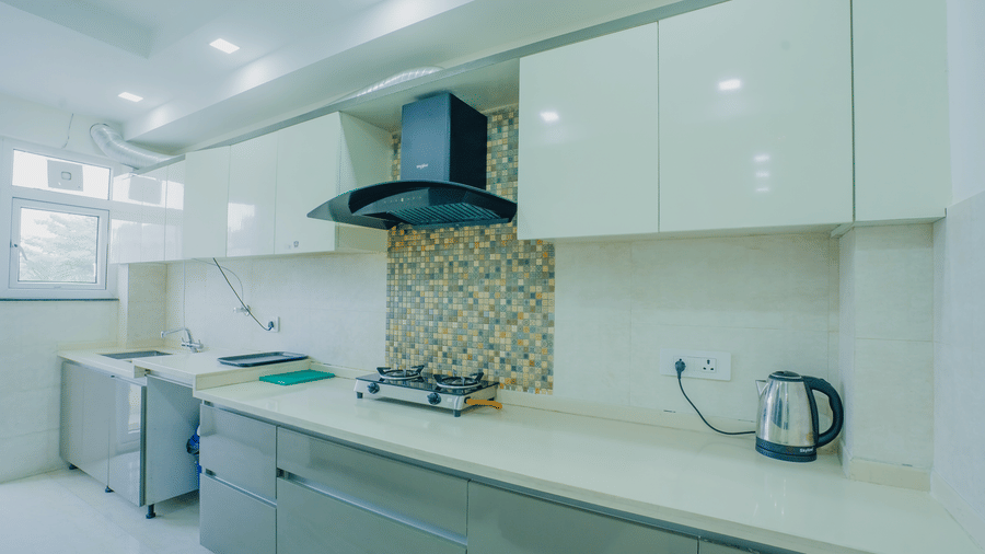 Kitchen of Lime Tree Hotels & Service Apartment Private Limited featuring white modular cabinetry, a hob, and a chimney.