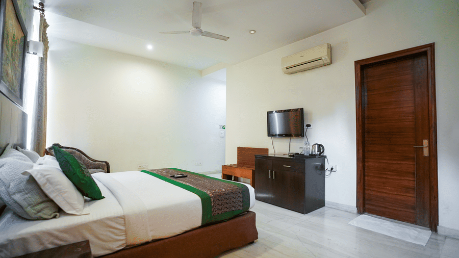 Bedroom of Lime Tree Hotels & Service Apartment Private Limited featuring a wooden door, a wall mounted television, and green bedding.
