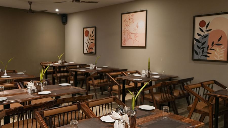 Multiple wooden tables and chairs with simple decor and botanical artwork on the wall at TGI Livancia Hillside, JC Nagar, Mysore
