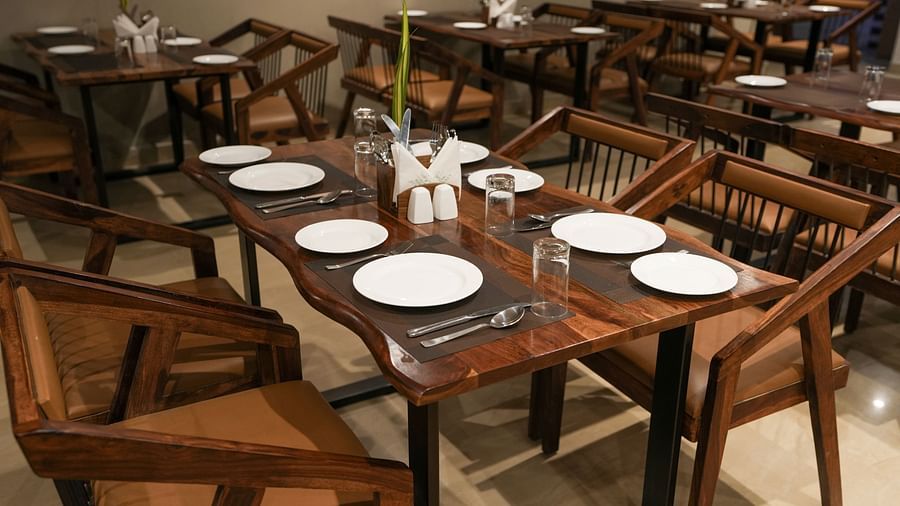 Close-up of a wooden table set for six with curved edges and modern wooden chairs at TGI Livancia Hillside, JC Nagar, Mysore
