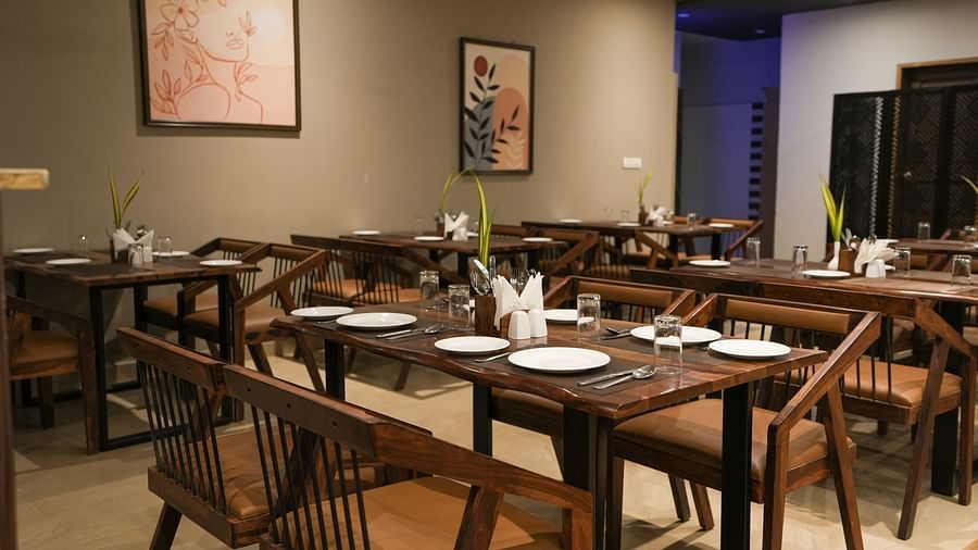 Wooden dining tables set with white plates, glasses, and cutlery in a warmly lit restaurant at TGI Livancia Hillside, JC Nagar, Mysore