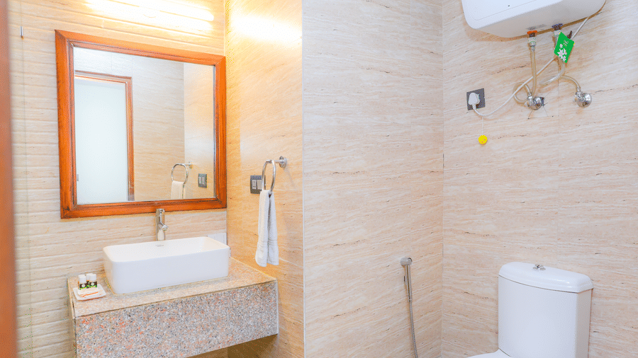 The western commode, wall-mounted heater, sink in the bathroom of a Suite With Balcony at Livbox, Dehradun.