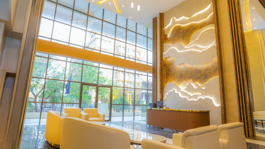 The lobby of Livbox, Dehradun, featuring a floor-to-ceiling glass window, high ceiling with a chandelier, a seating area with sofas below it, and a reception desk.