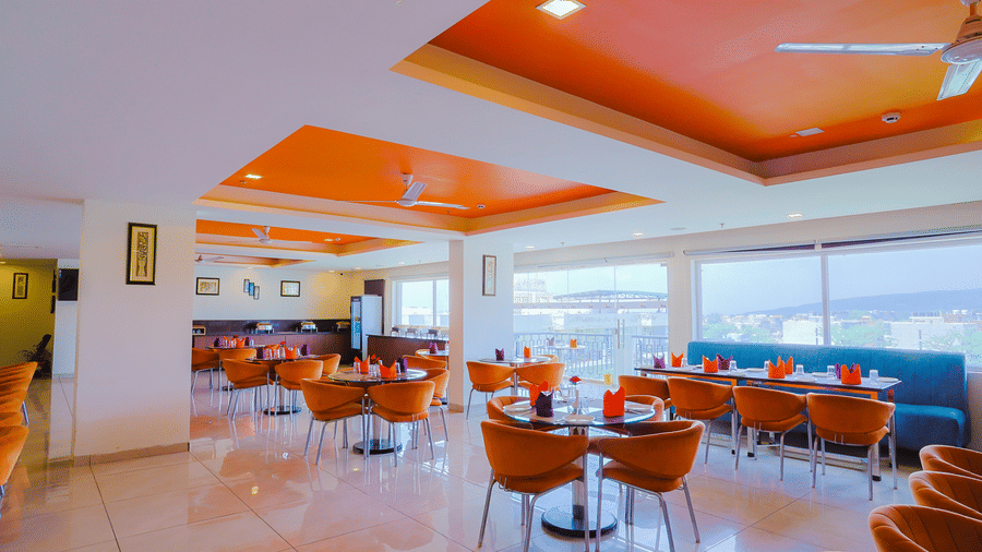 Cafe Treat at Livbox, Dehradun, furnished with dining tables and cushioned sofas, offering view of the city through the floor-to-ceiling glass windows.