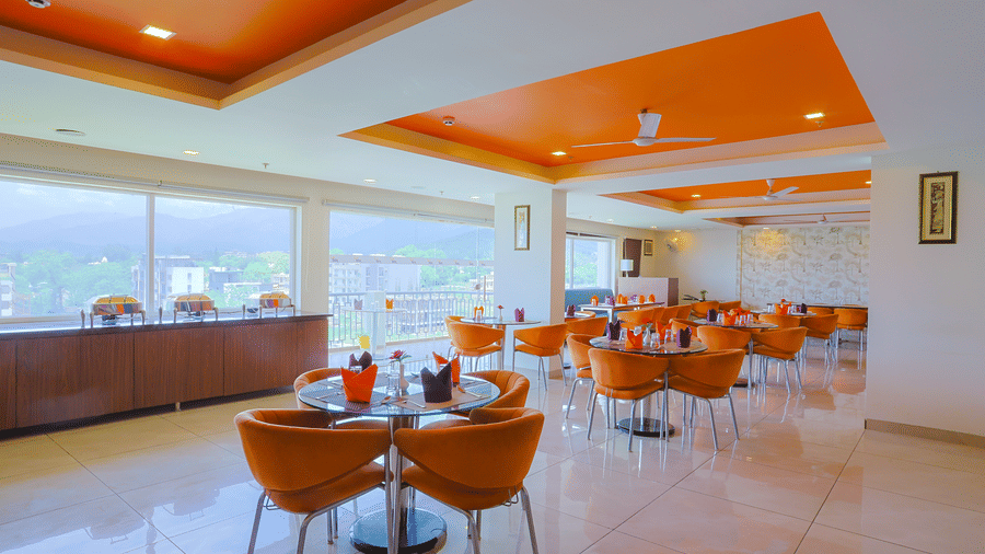 The chafing dishes on a counter placed in front of big glass windows, with dining tables arranged spaciously.