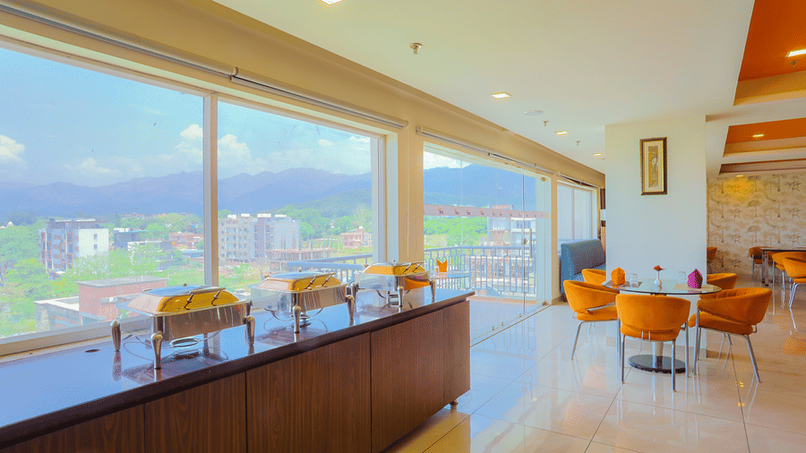 The chafing dishes on a counter placed in front of the big glass windows that offer view of the surroundings.