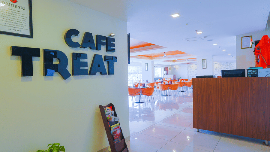 Cafe Treat restaurant entrance at Livbox, Dehradun, with dining tables and chairs, a reception desk, wall signage, and a magazine stand near the doorway.