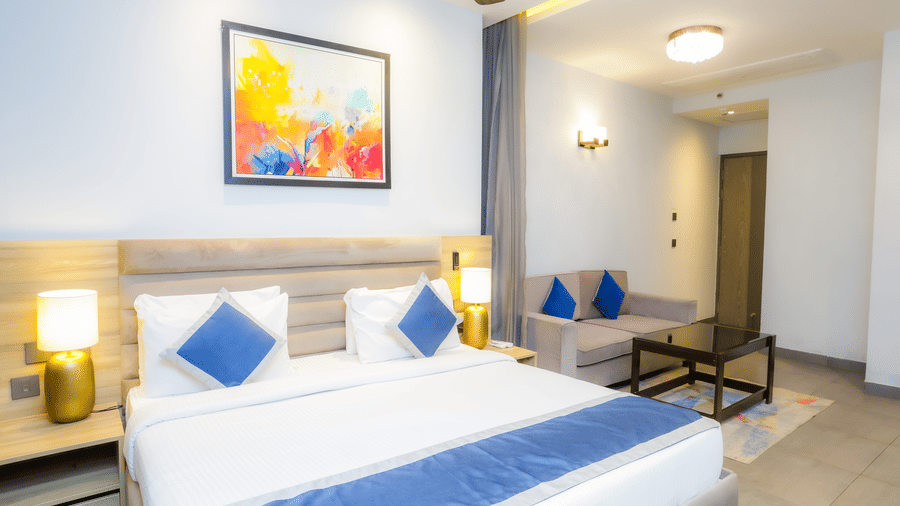 Bedroom with modern decor, an artwork, bedside lamps, and a seating area in Livbox Supernova, Noida.