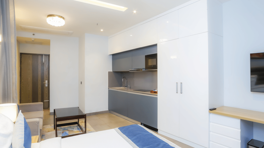 Bright bedroom with double bed, a wardrobe, seating area, and a kitchenette in Livbox Supernova, Noida.