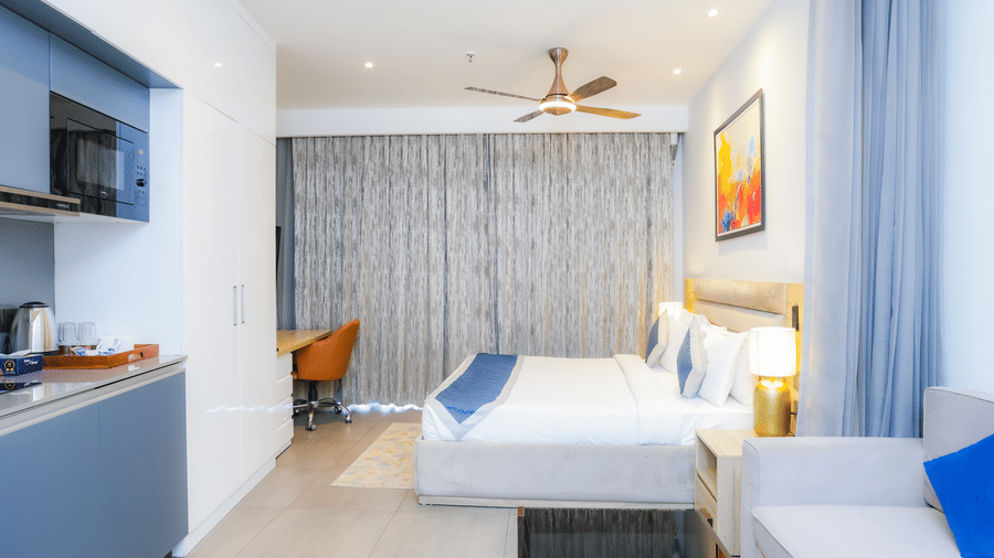 Contemporary bedroom with king size bed and blue curtains at Livbox Supernova, Noida.