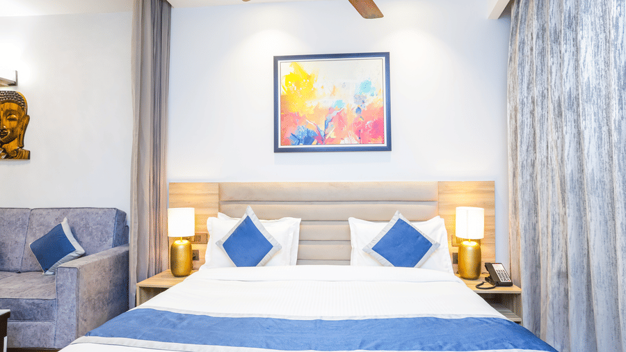 Elegant bedroom with plush king size bed, bedside lamps, and framed artwork at Livbox Supernova, Noida.
