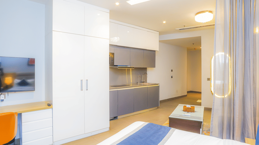 Spacious studio bedroom featuring a king size bed, work desk, wardrobe, and kitchenette at Livbox Supernova, Noida.